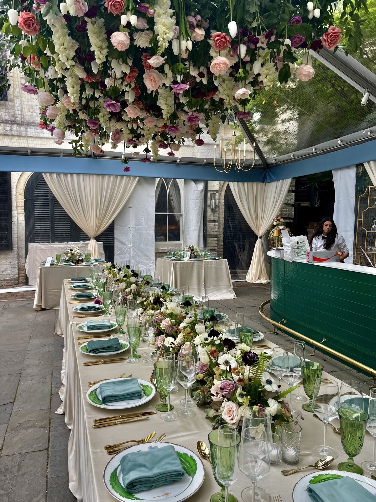 Hanging installation of roses, tulips, and wisteria above a long courtyard dining table
