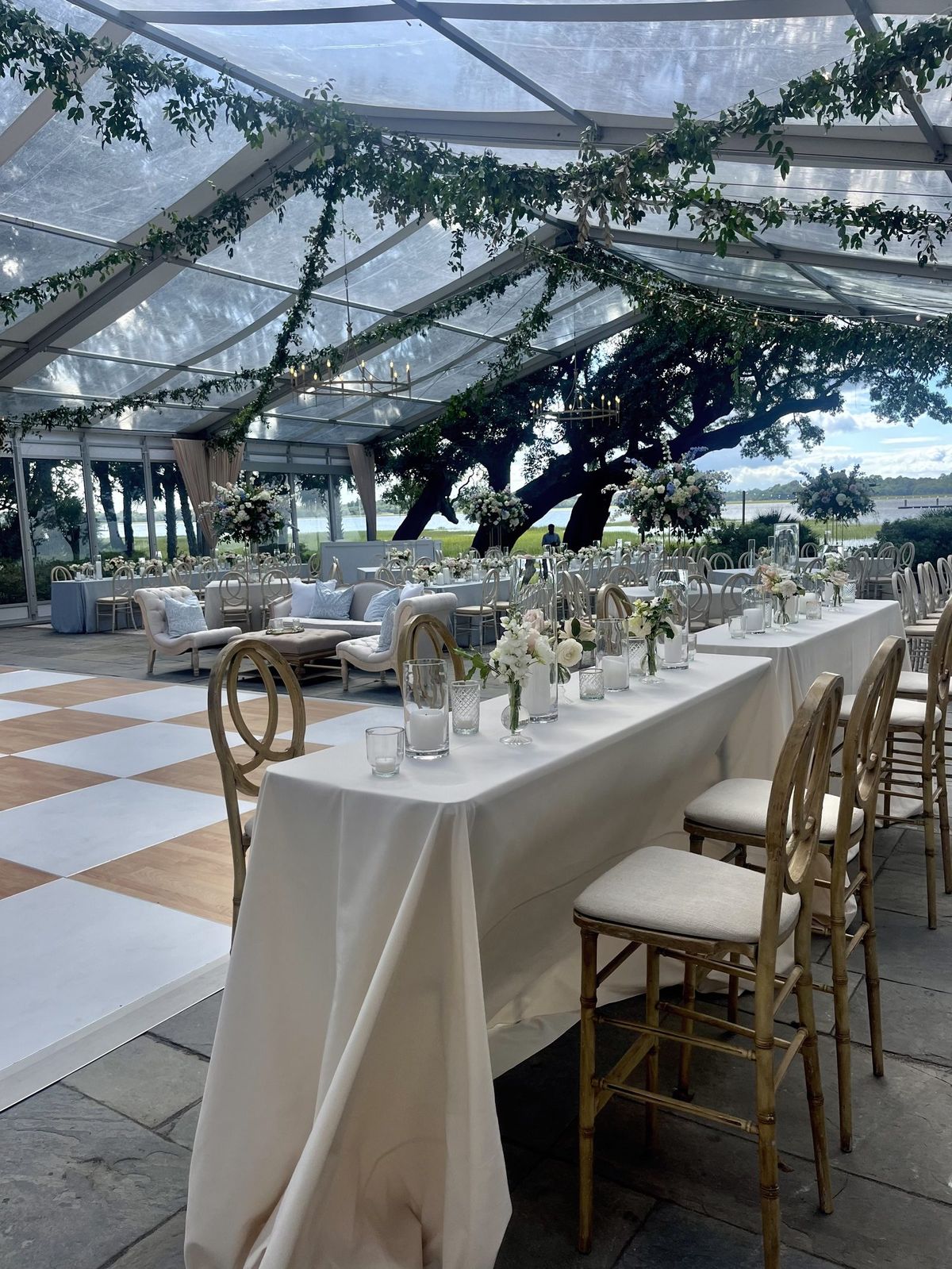 Clear-top tent reception beneath a live oak overlooking the water, with a checkerboard dance floor and lounge seating